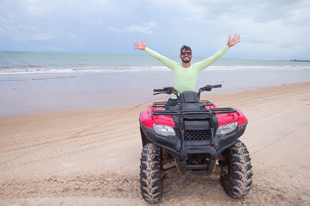 Homem jovem curtindo férias andando de quadriciclo sobre dunas
