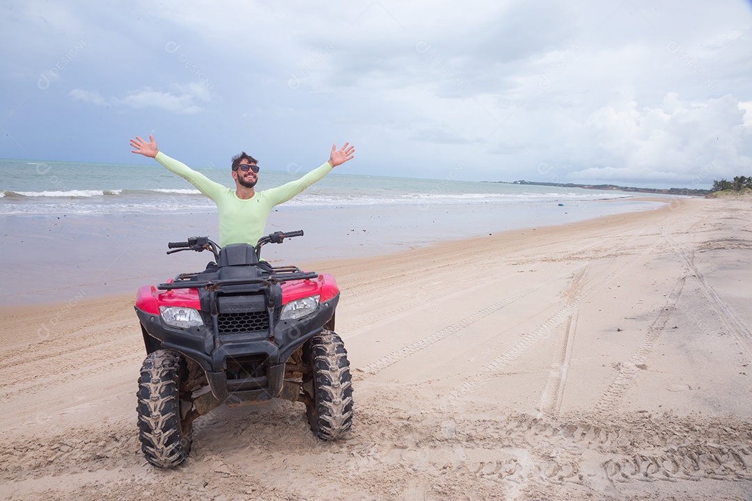 Homem jovem curtindo férias andando de quadriciclo sobre dunas