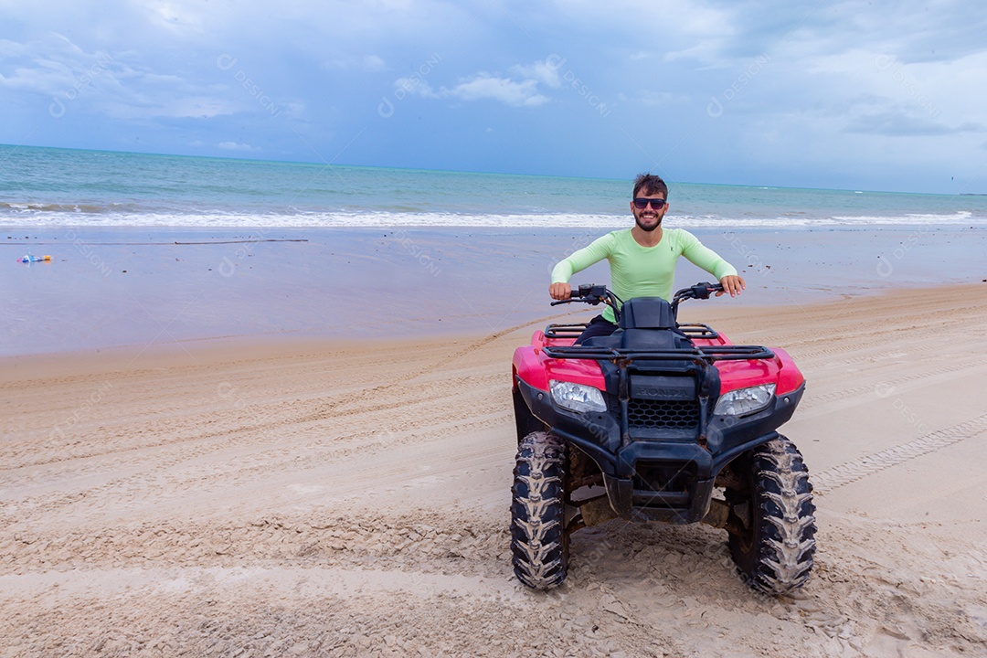 Homem jovem curtindo férias andando de quadriciclo sobre dunas