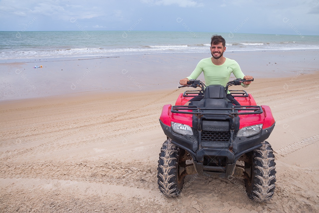 Homem jovem curtindo férias andando de quadriciclo sobre dunas