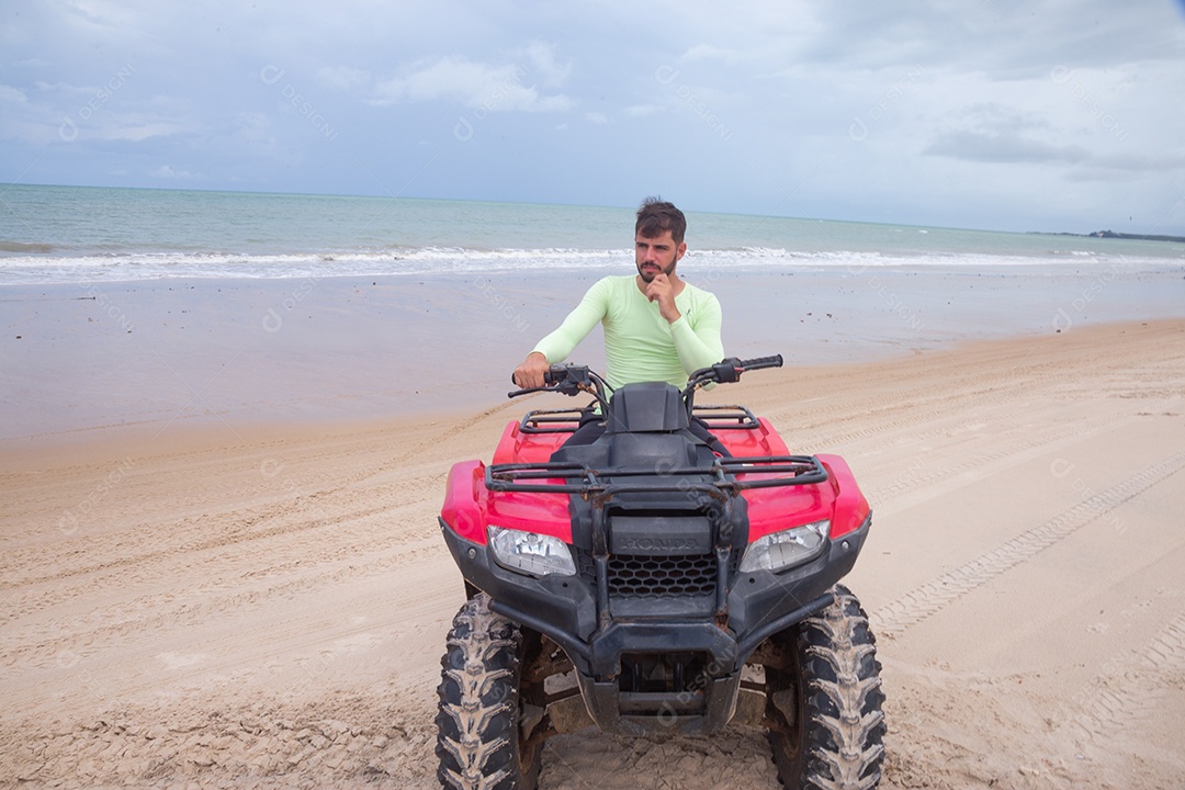 Homem jovem curtindo férias andando de quadriciclo sobre dunas