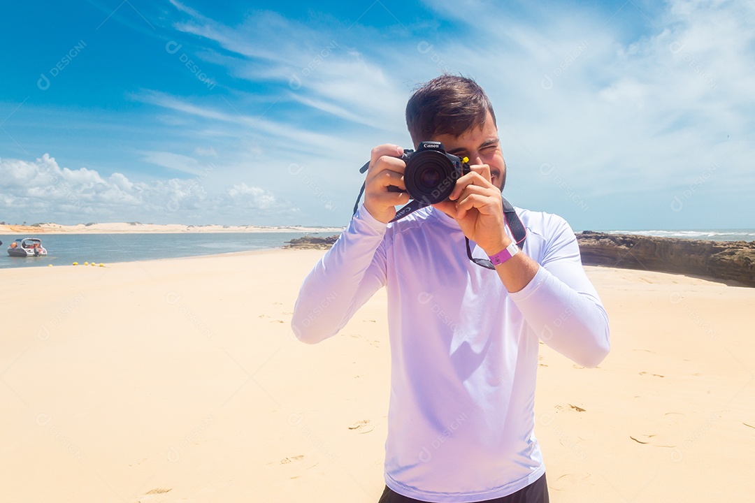 Homem jovem segurando câmera fotográfica fotografando praia