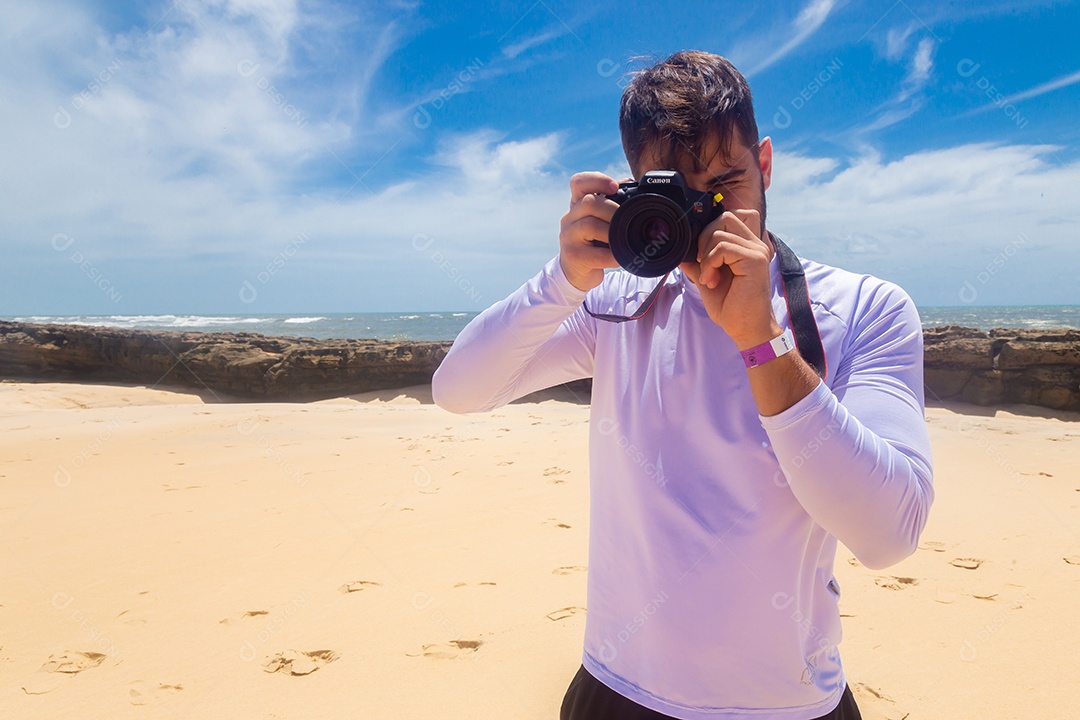 Homem jovem segurando câmera fotográfica fotografando praia