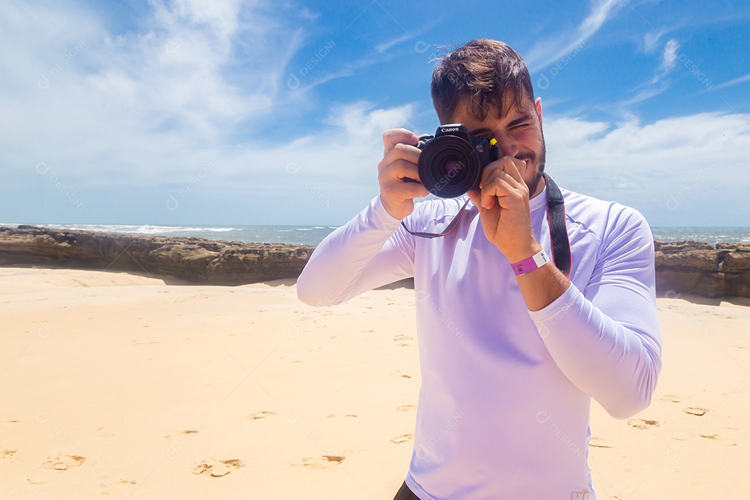 Homem jovem segurando câmera fotográfica fotografando praia