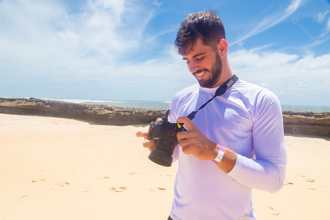 Homem jovem segurando câmera fotográfica fotografando praia