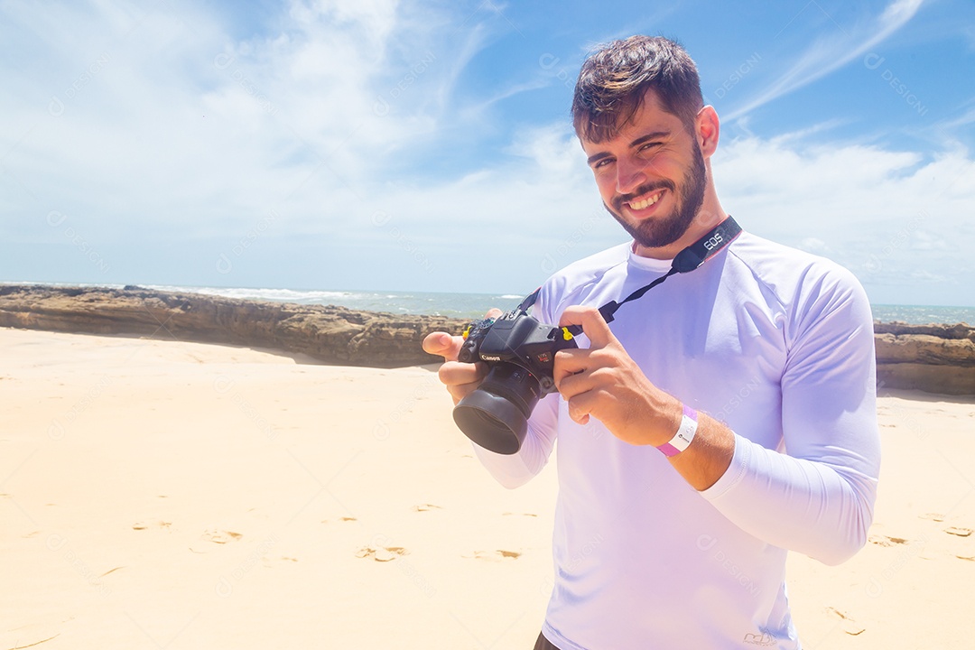 Homem jovem segurando câmera fotográfica fotografando praia