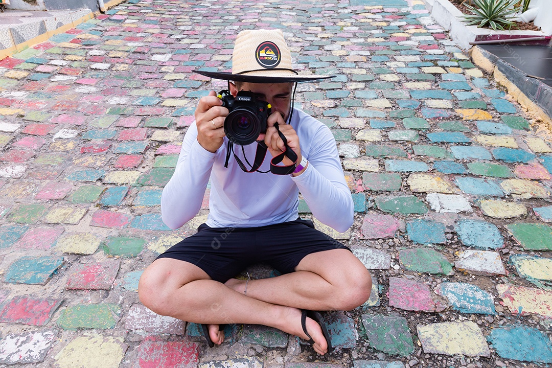 Homem jovem sentado no chão tirando fotos usando câmera fotográfica