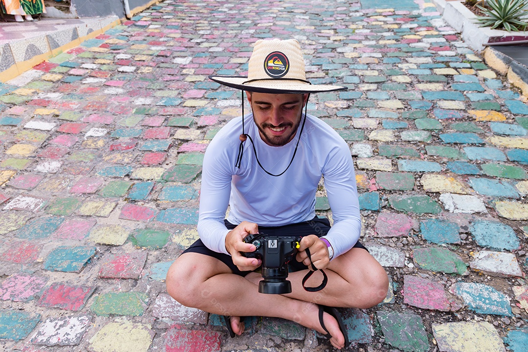 Homem jovem sentado no chão tirando fotos usando câmera fotográfica