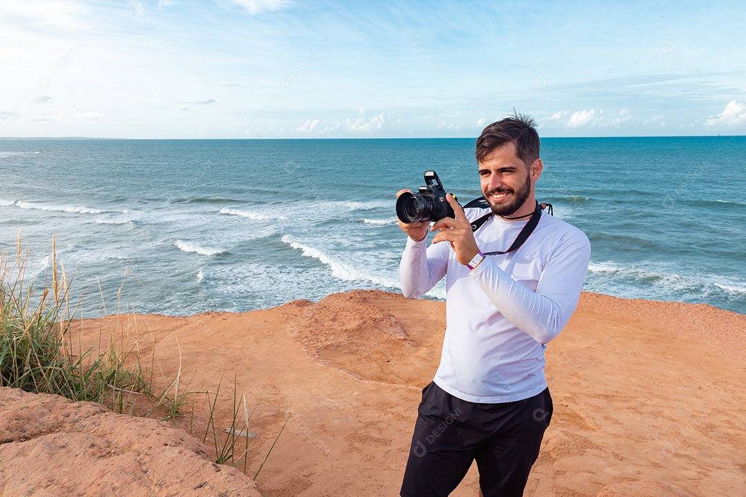 Homem jovem segurando câmera fotográfica fotografando praia