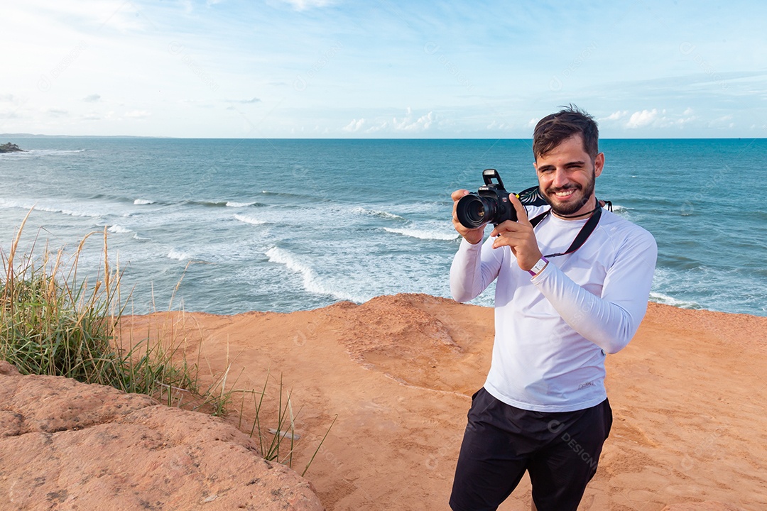 Homem jovem segurando câmera fotográfica fotografando praia