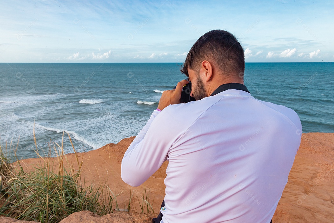 Homem jovem segurando câmera fotográfica fotografando praia