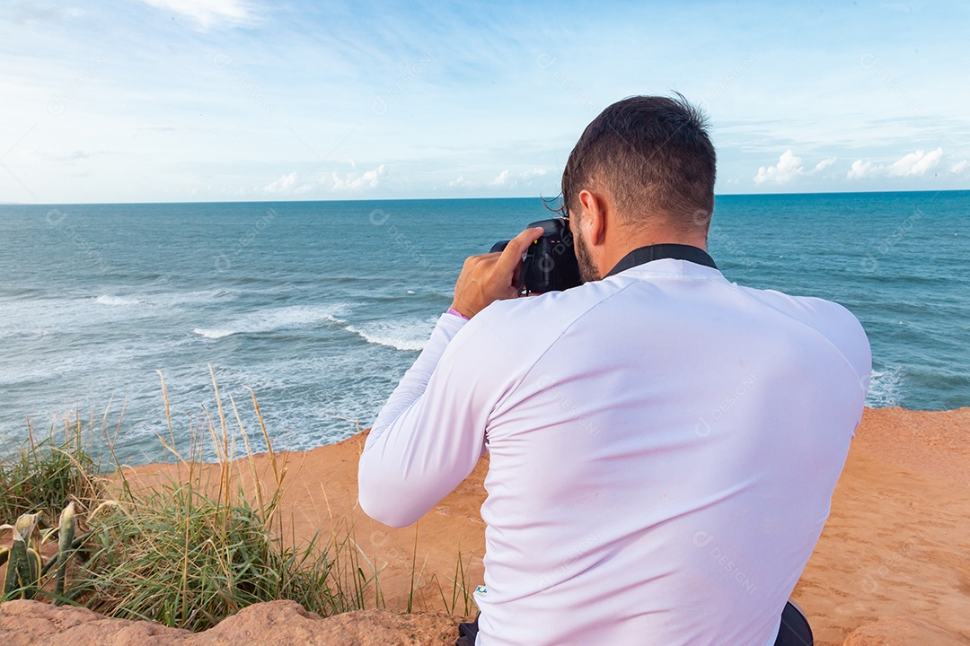 Homem jovem segurando câmera fotográfica fotografando praia