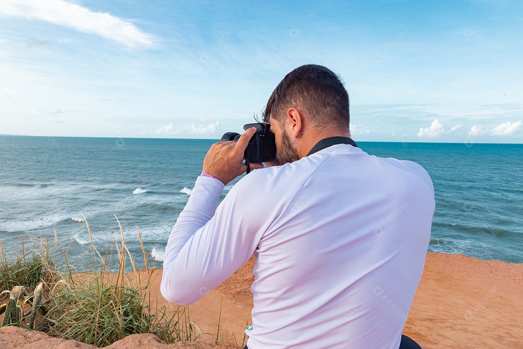 Homem jovem segurando câmera fotográfica fotografando praia