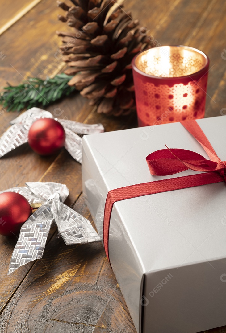 Caixa de presente, bolas de natal, caixa de presente, pinha, vela e arco sobre mesa de madeira.