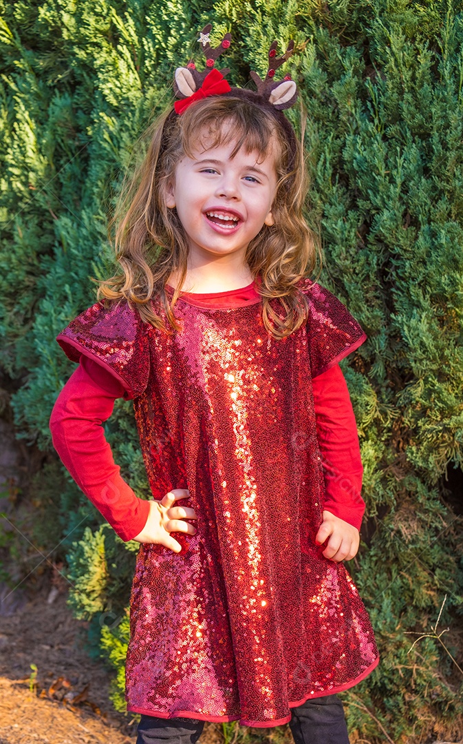 Linda garotinha loira posando em roupas de Natal e fundo de pinheiros.