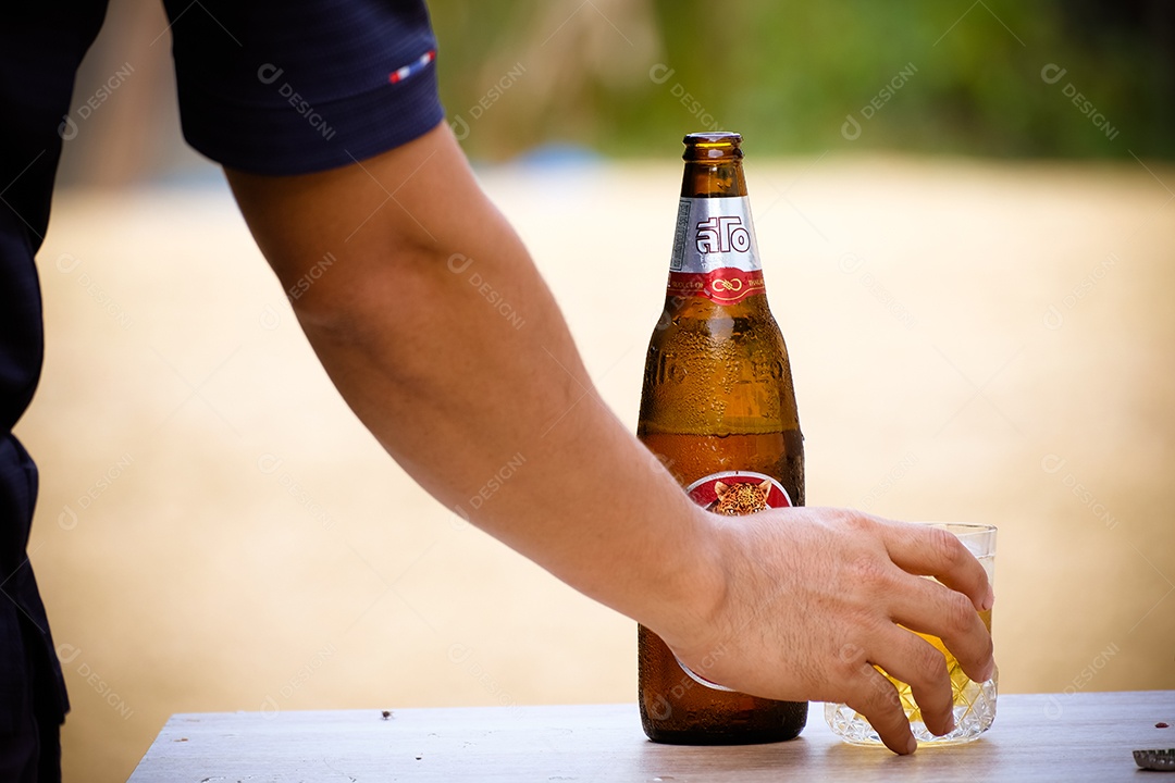 Mãos de pessoa pegando copo de cerveja garrafa long neck sobre uma mesa branca