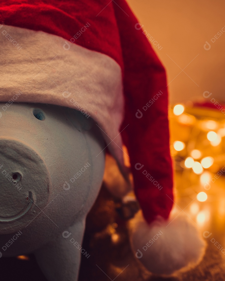 Cofrinho com chapéu de Papai Noel em fundo desfocado de Natal com enfeites, presentes e luz. Espaço para texto.