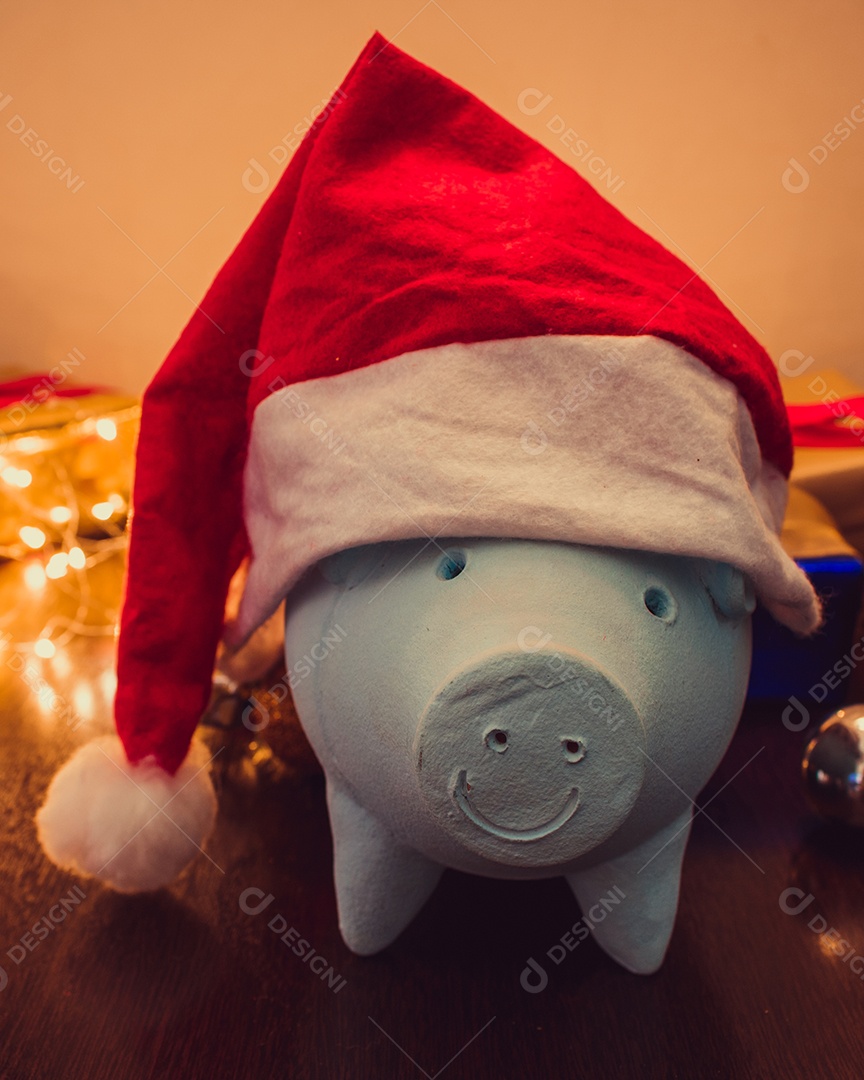 Cofrinho com chapéu de Papai Noel em fundo desfocado de Natal com enfeites, presentes e luz. Espaço para texto.