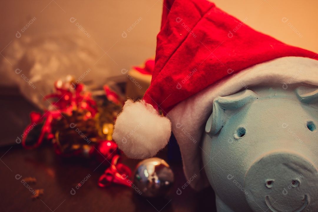 Cofrinho com chapéu de Papai Noel em fundo desfocado de Natal com enfeites, presentes e luz. Espaço para texto.