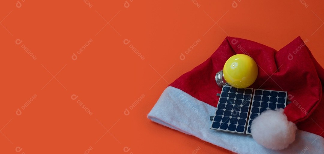 Chapéu de Papai Noel de Natal com painel solar fotovoltaico e lâmpada isolada em fundo laranja.