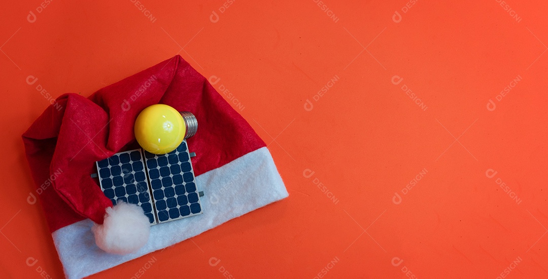 Chapéu de Papai Noel de Natal com painel solar fotovoltaico e lâmpada isolada em fundo laranja.