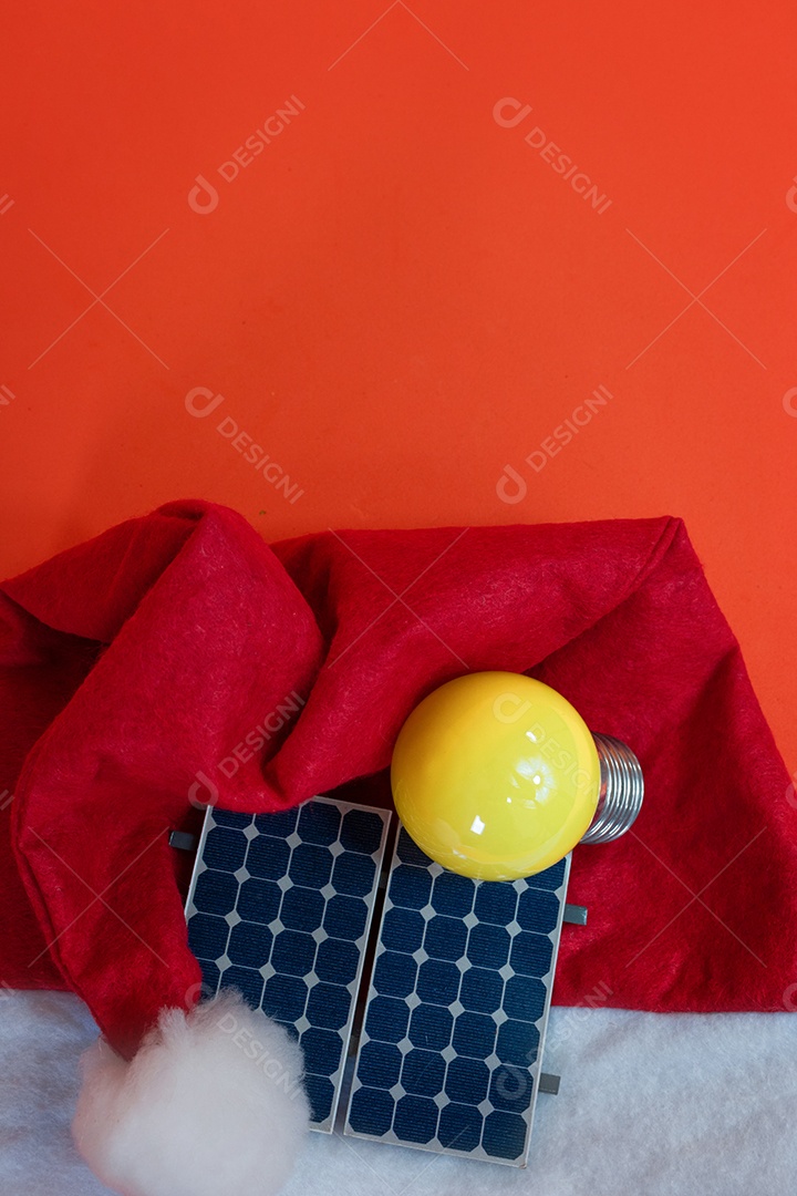 Chapéu de Papai Noel de Natal com painel solar fotovoltaico e lâmpada isolada em fundo laranja.