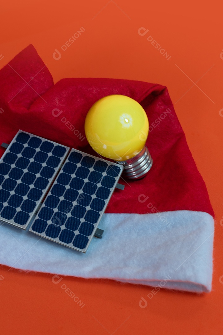 Chapéu de Papai Noel de Natal com painel solar fotovoltaico e lâmpada isolada em fundo laranja.