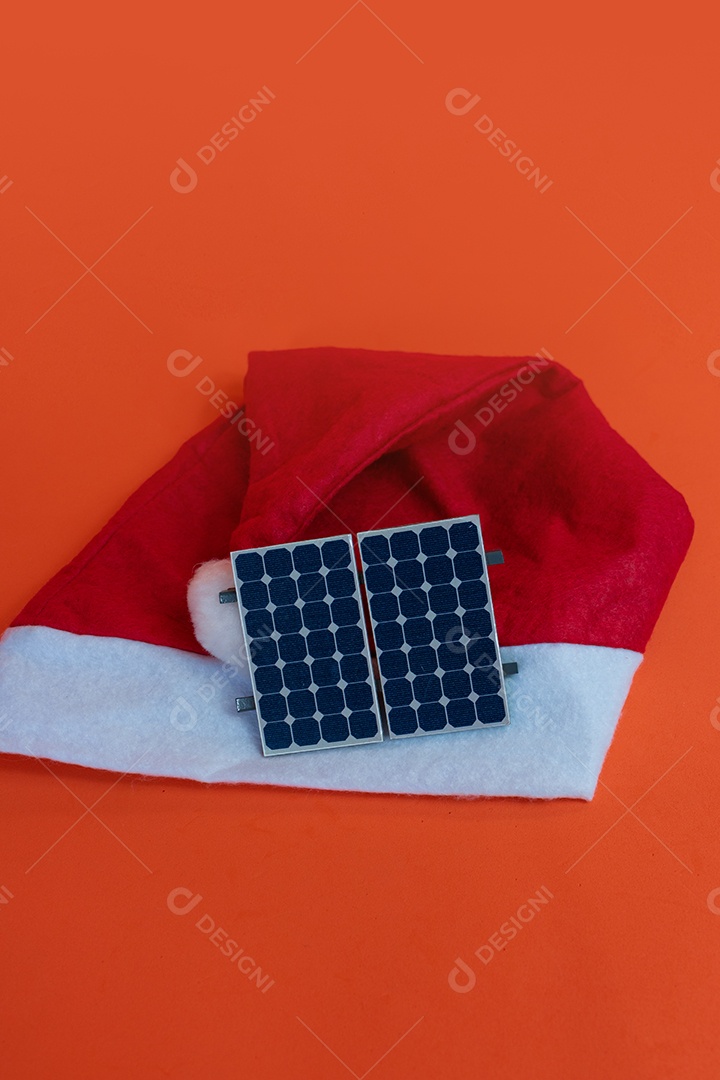 Chapéu de Papai Noel de Natal com painel solar fotovoltaico e lâmpada isolada em fundo laranja.