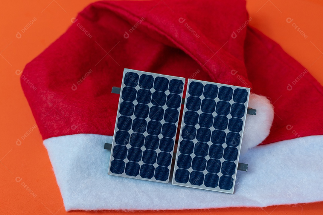 Chapéu de Papai Noel de Natal com painel solar fotovoltaico e lâmpada isolada em fundo laranja.