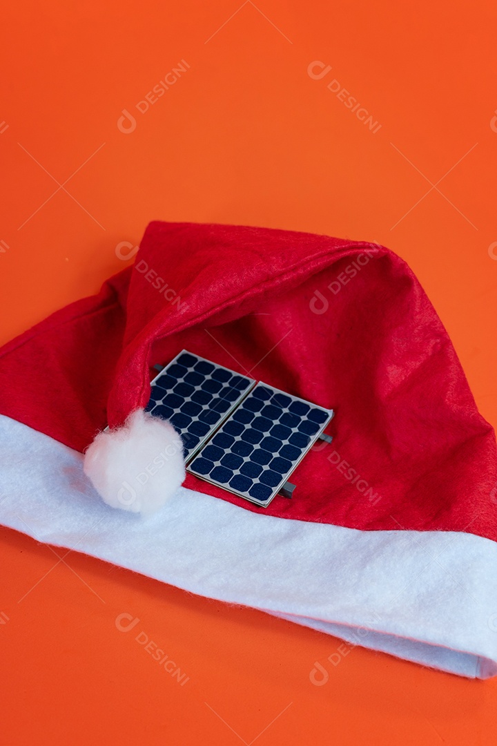 Chapéu de Papai Noel de Natal com painel solar fotovoltaico e lâmpada isolada em fundo laranja.