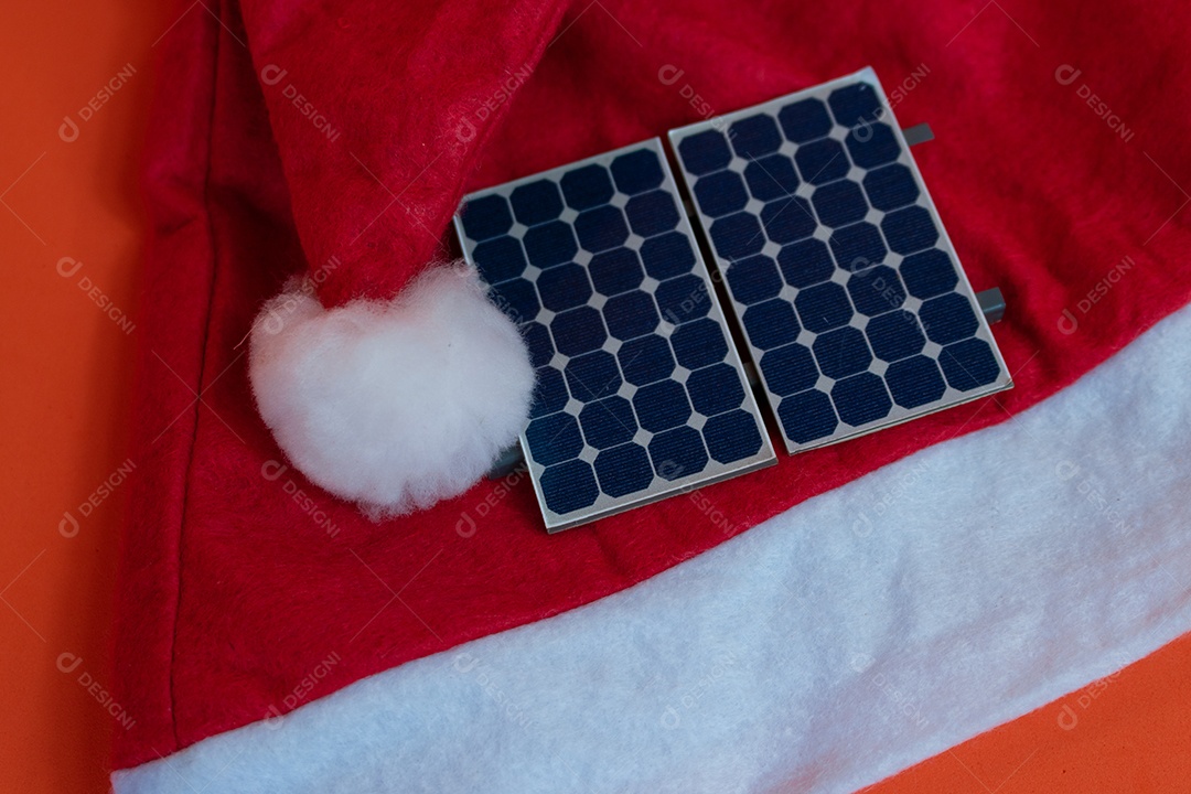 Chapéu de Papai Noel de Natal com painel solar fotovoltaico e lâmpada isolada em fundo laranja.