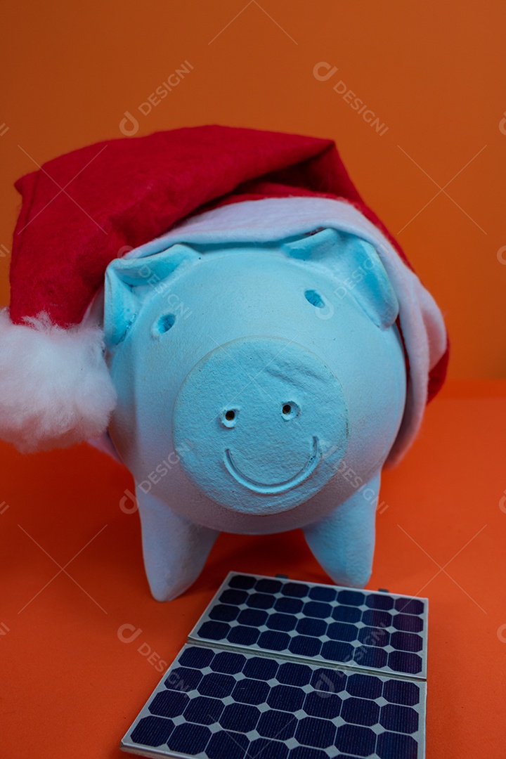 Moedas do cofrinho com chapéu de Natal de Papai Noel, painel solar fotovoltaico e lâmpada isolada em fundo laranja.