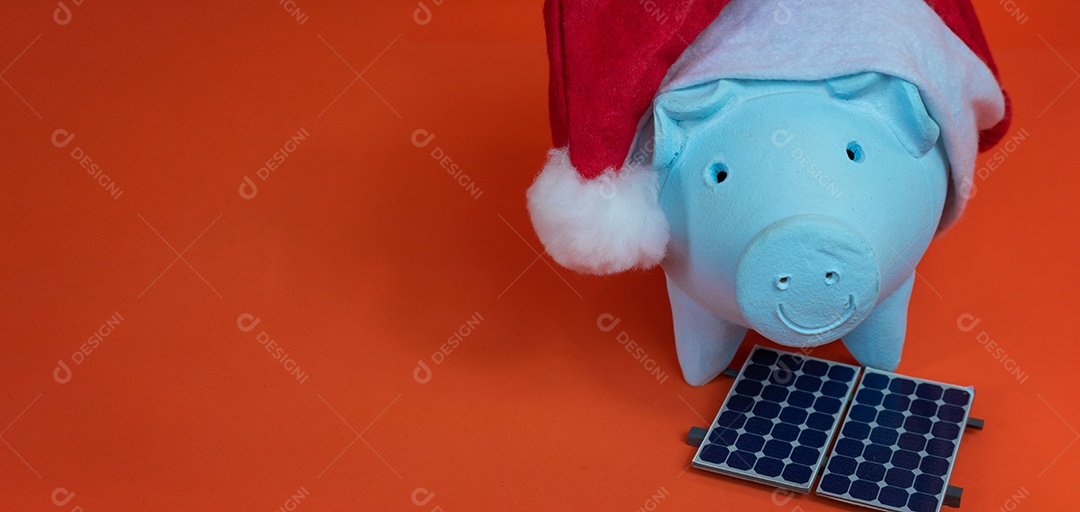 Moedas do cofrinho com chapéu de Natal de Papai Noel, painel solar fotovoltaico e lâmpada isolada em fundo laranja.
