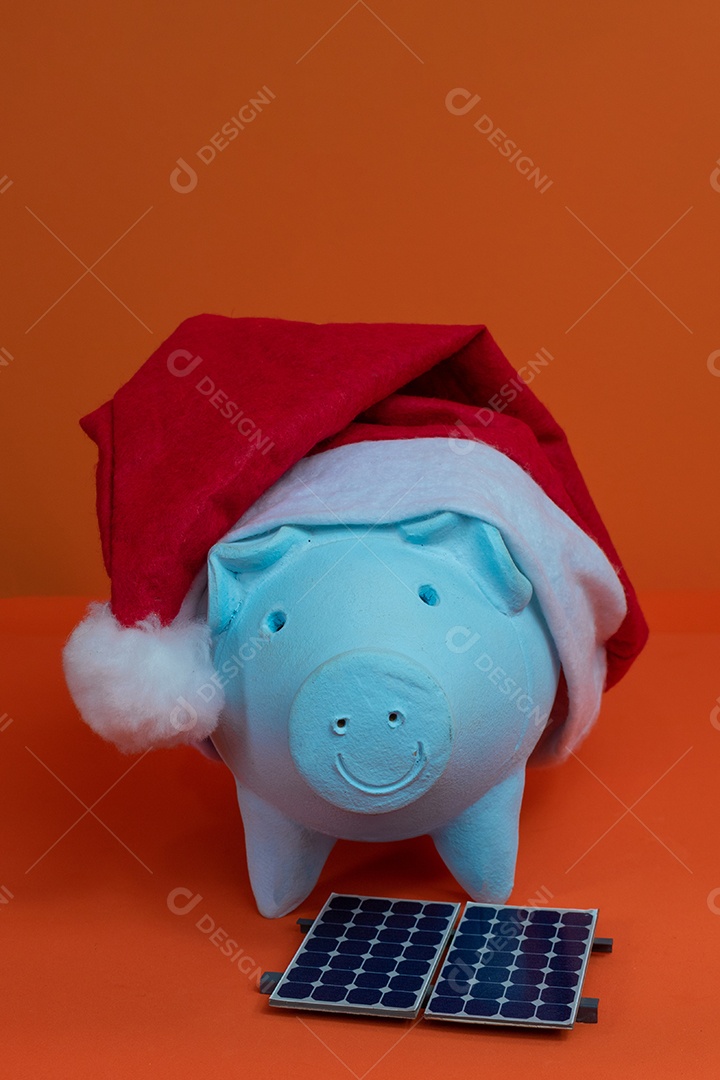 Moedas do cofrinho com chapéu de Natal de Papai Noel, painel solar fotovoltaico e lâmpada isolada em fundo laranja.