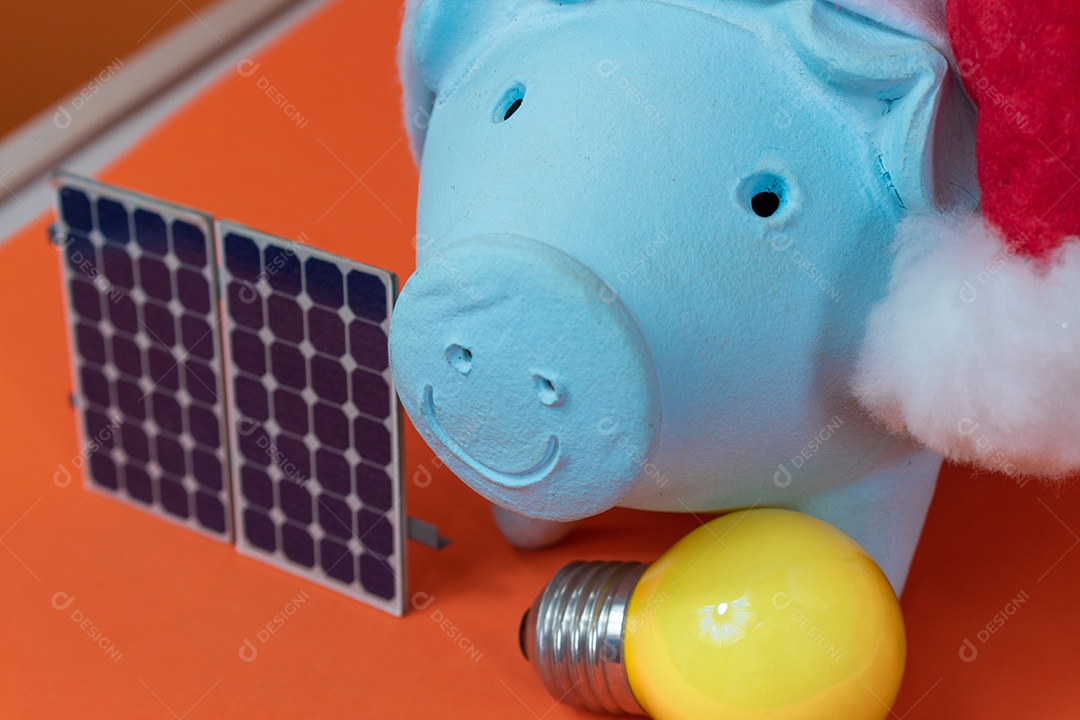 Moedas do cofrinho com chapéu de Natal de Papai Noel, painel solar fotovoltaico e lâmpada isolada em fundo laranja.