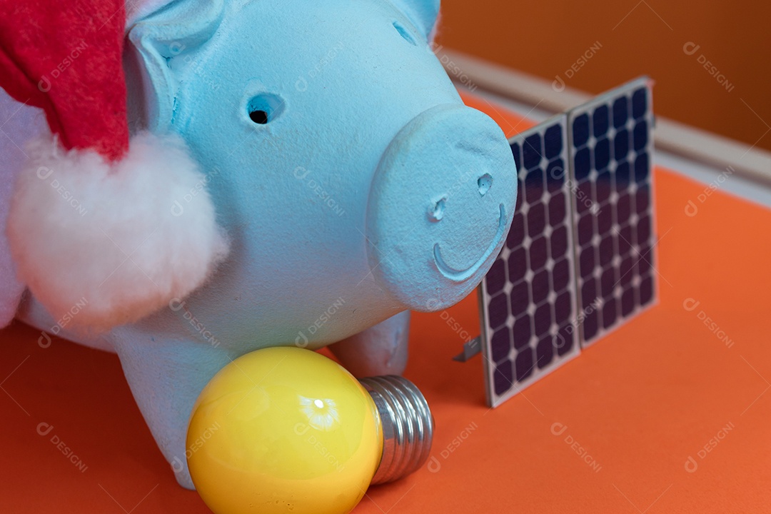 Moedas do cofrinho com chapéu de Natal de Papai Noel, painel solar fotovoltaico e lâmpada isolada em fundo laranja.