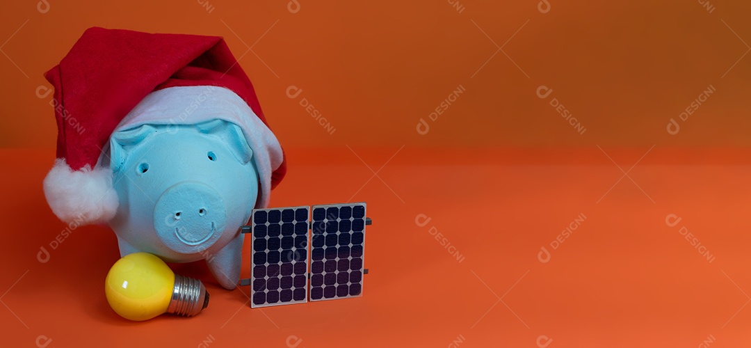 Moedas do cofrinho com chapéu de Natal de Papai Noel, painel solar fotovoltaico e lâmpada isolada em fundo laranja.