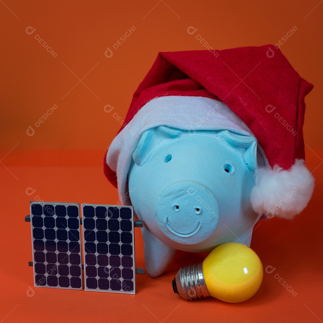 Moedas do cofrinho com chapéu de Natal de Papai Noel, painel solar fotovoltaico e lâmpada isolada em fundo laranja.