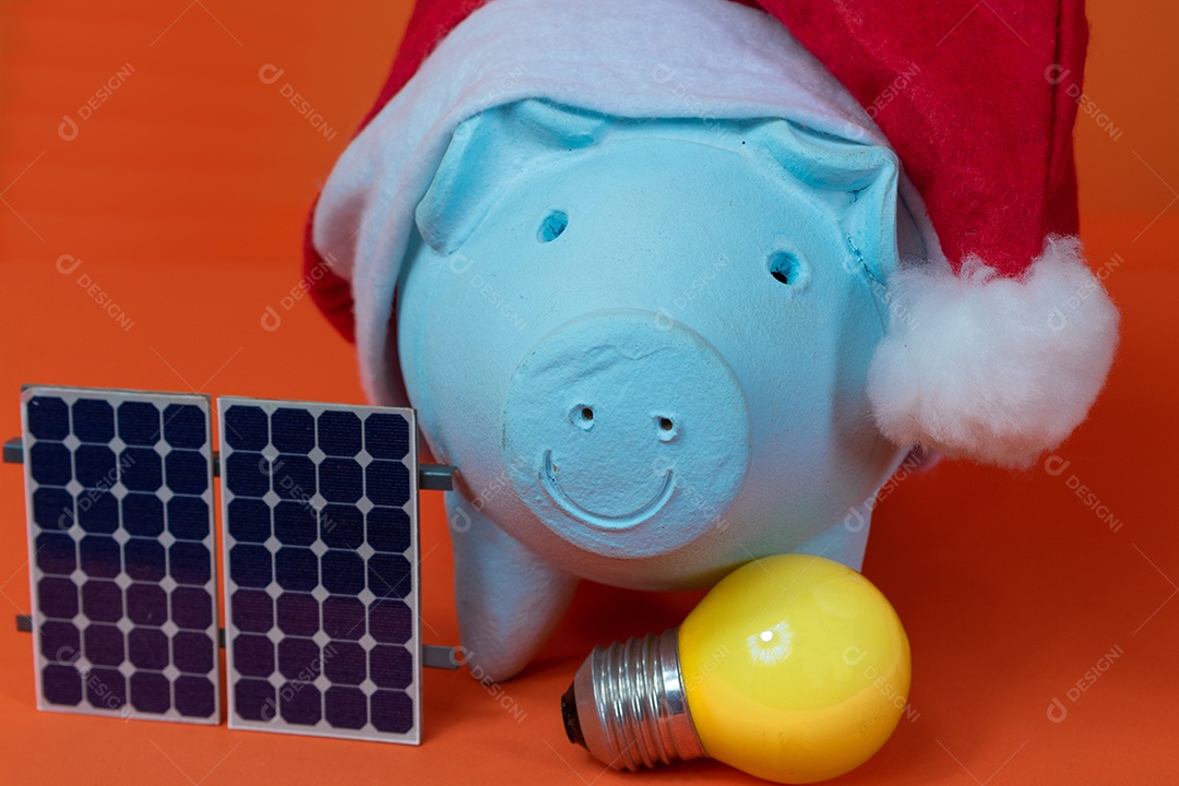 Moedas do cofrinho com chapéu de Natal de Papai Noel, painel solar fotovoltaico e lâmpada isolada em fundo laranja.