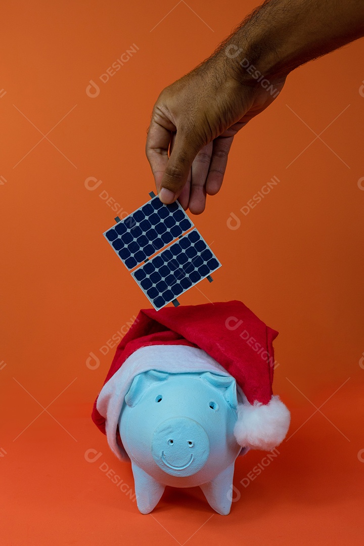 Moedas do cofrinho com chapéu de Natal de Papai Noel, painel solar fotovoltaico e lâmpada isolada em fundo laranja.