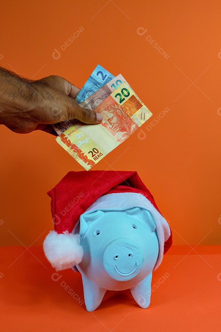 Moedas do cofrinho com chapéu de Natal de Papai Noel, painel solar fotovoltaico e lâmpada isolada em fundo laranja.