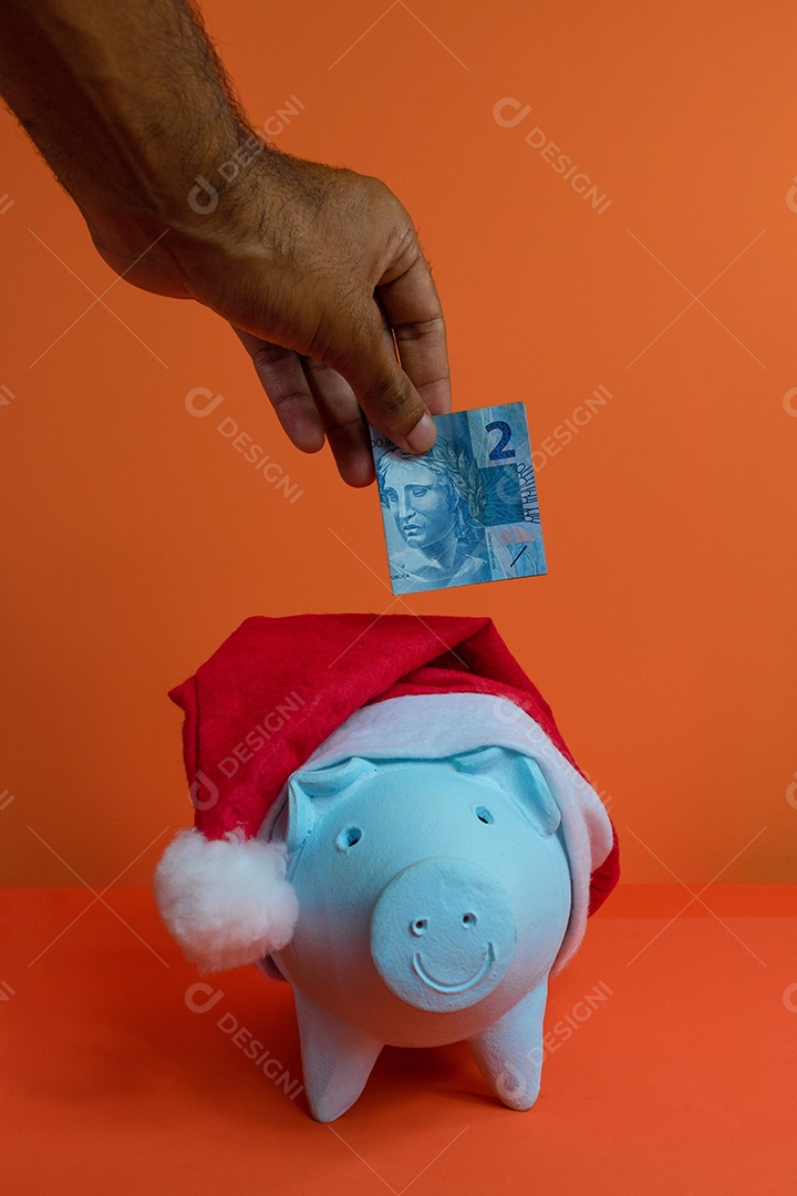 Moedas do cofrinho com chapéu de Natal de Papai Noel, painel solar fotovoltaico e lâmpada isolada em fundo laranja.
