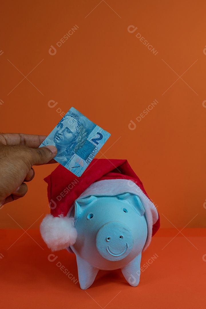 Moedas do cofrinho com chapéu de Natal de Papai Noel, painel solar fotovoltaico e lâmpada isolada em fundo laranja.