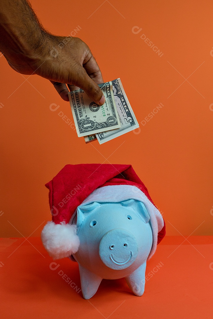 Moedas do cofrinho com chapéu de Natal de Papai Noel, painel solar fotovoltaico e lâmpada isolada em fundo laranja.