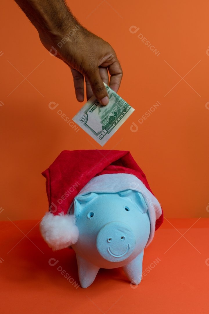Moedas do cofrinho com chapéu de Natal de Papai Noel, painel solar fotovoltaico e lâmpada isolada em fundo laranja.