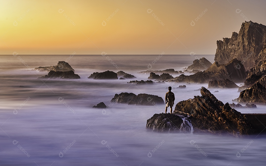 Young man watching the sunset on the rocks by the sea enjoying