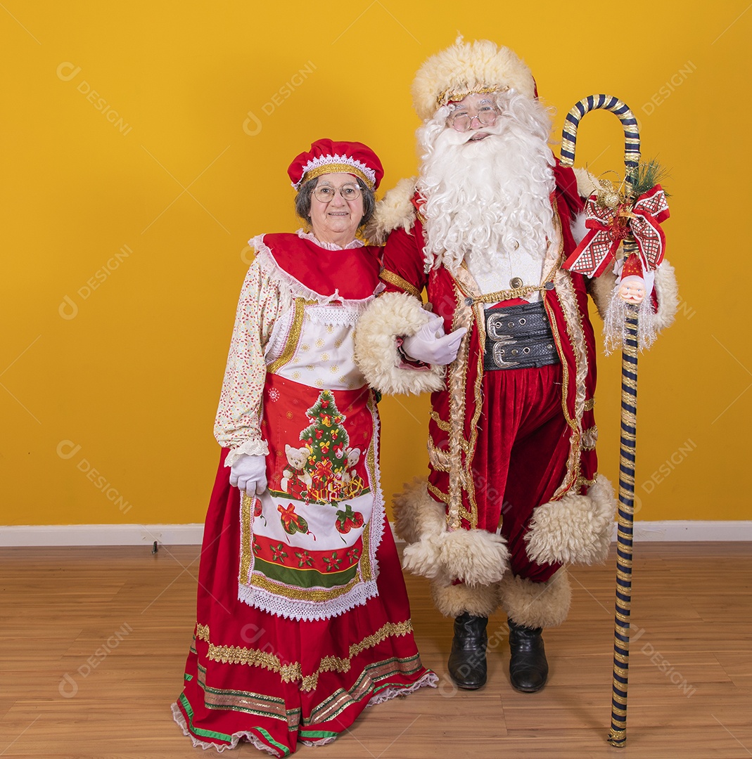 Lindo Casal Papai Noel ao lado de Mamãe Noel sobre fundo isolado amarelo