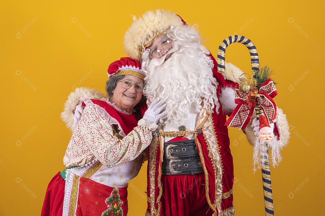Lindo Casal Papai Noel ao lado de Mamãe Noel sobre fundo isolado amarelo