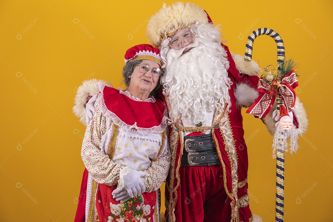 Lindo Casal Papai Noel ao lado de Mamãe Noel sobre fundo isolado amarelo