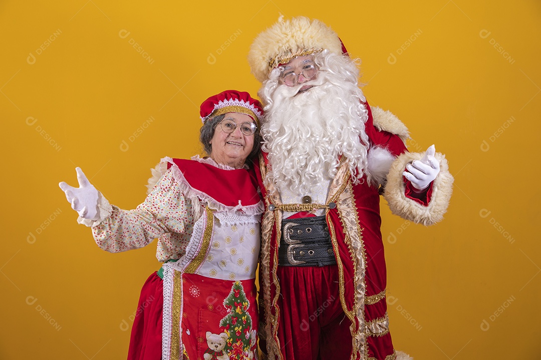Lindo Casal Papai Noel ao lado de Mamãe Noel sobre fundo isolado amarelo